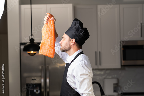 A chef is holding a piece of salmon in his hand and wearing a black hat. High quality photoA chef is holding a piece of salmon in his hand and wearing a black hat. Concept expertise in the kitchen photo