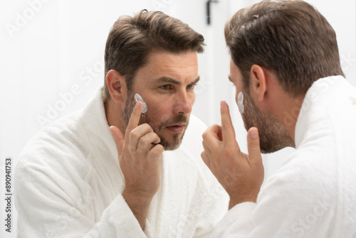 A man is applying lotion to his face in front of a mirror. Concept of self-care and personal grooming