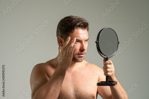 guy standing in modern bathroom at home. Male Beauty And Haircare Routine. Handsome Man Touching Hair Looking In The Mirror After Shower, Smiling To His Reflection Standing In Modern Bathroom