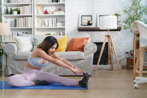young attractive asian woman in sportswear sitting on yoga mat stretching legs before fitness training in the living room