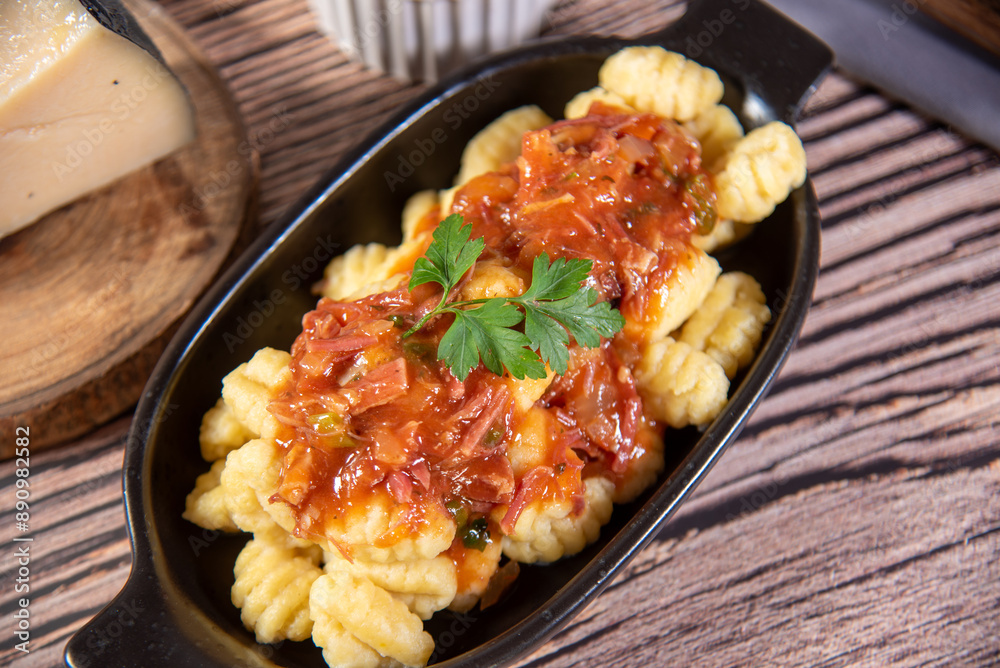 Gnocchi with parmesan cheese on the side in tomato sauce on a wooden table with preparation components around it Gnocchi with parmesan cheese on the side in tomato sauce on a wooden table with preparation components around it