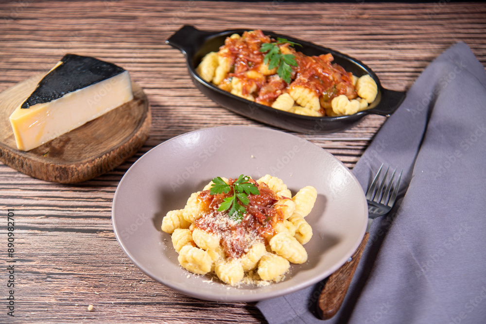 Gnocchi with grated parmesan cheese in tomato sauce on a wooden table with preparation components around it Gnocchi with grated parmesan cheese in tomato sauce on a wooden table with preparation components around it
