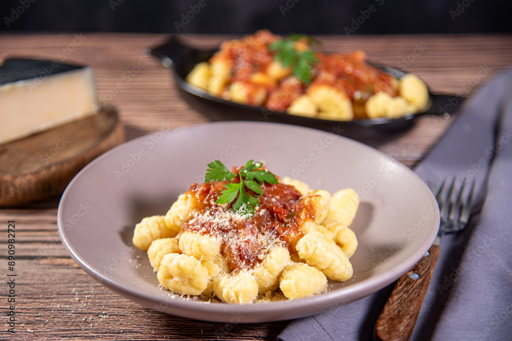 Gnocchi with grated parmesan cheese in tomato sauce on a wooden table with preparation components around it Gnocchi with grated parmesan cheese in tomato sauce on a wooden table with preparation components around it