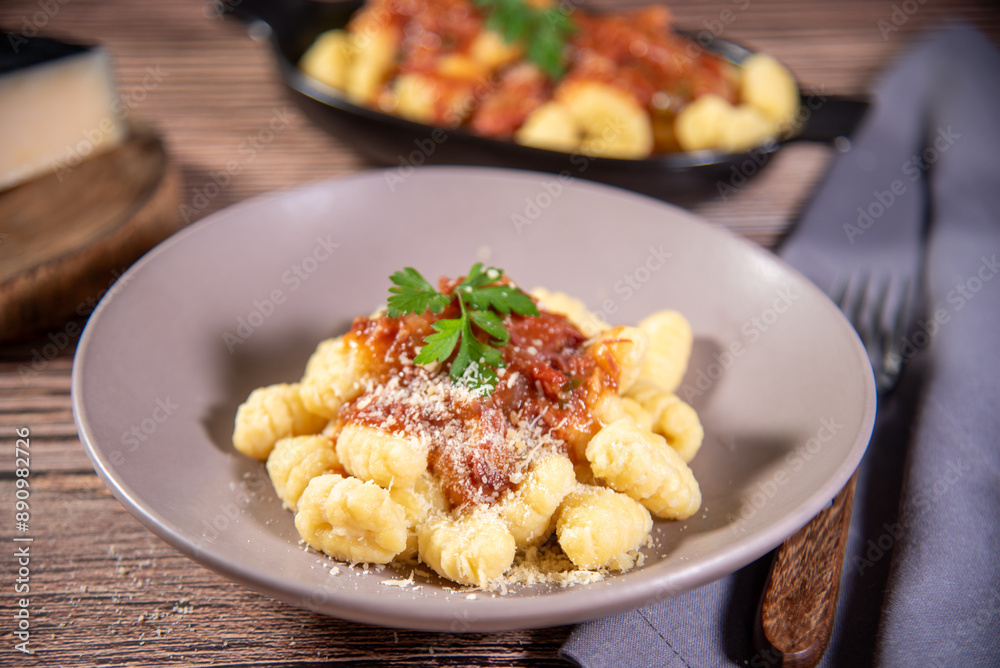 Gnocchi with grated parmesan cheese in tomato sauce on a wooden table with preparation components around it Gnocchi with grated parmesan cheese in tomato sauce on a wooden table with preparation components around it