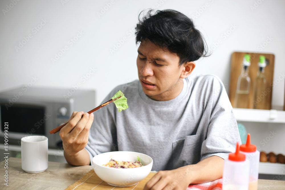Unhappy Asian Young Man Showing Not Delicious While Holding Vegetable With Chopstick Unhappy Asian Young Man Showing Not Delicious While Holding Vegetable With Chopstick