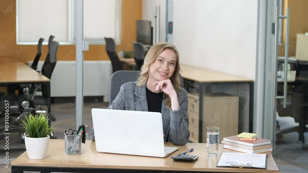 Beautiful young businesswoman sitting at table in office. Woman smiling while working in her laptop in a modern office. Beautiful young businesswoman sitting at table in office. Woman smiling while working in her laptop in a modern office.