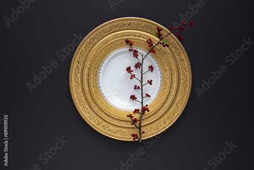 Close up and top angle view of Ilex serrata branch with red fruits on stacked round golden ceramic dish and black floor, South Korea
 photo