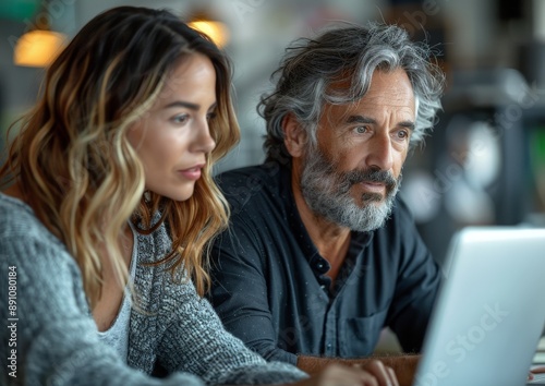 Two busy colleagues working together talking using laptop in office. Middle aged Latin female manager teaching young male worker looking at computer discussing business plan at office meeting