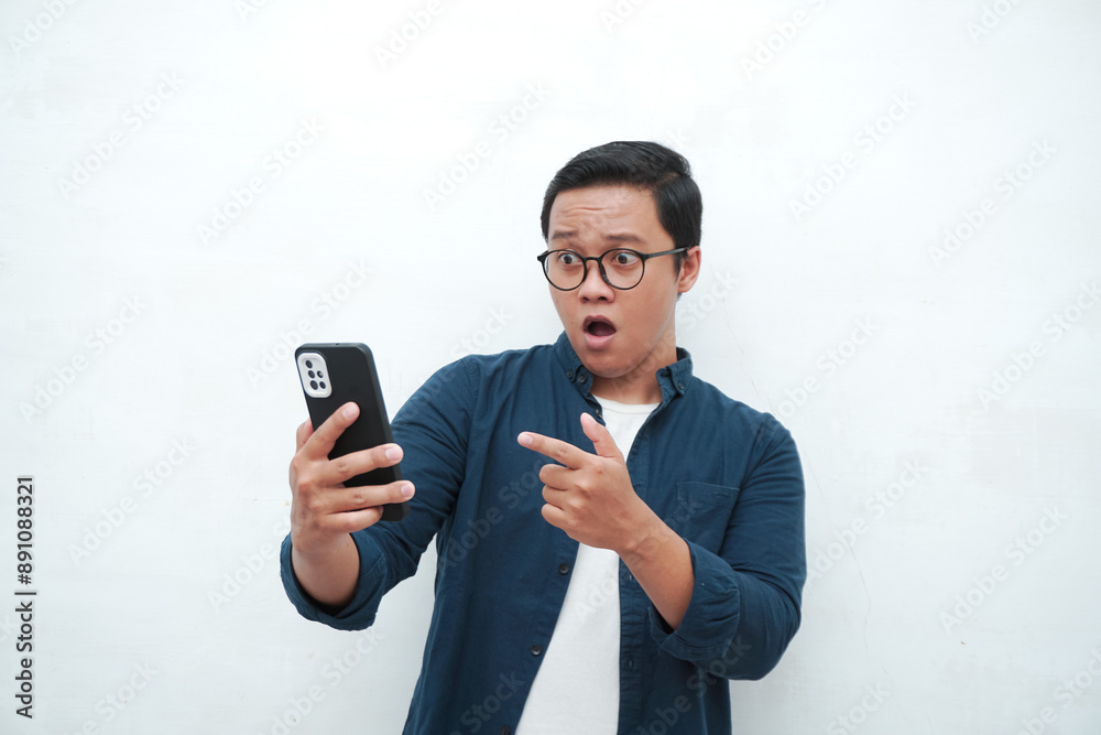 Young Asian man looking smartphone with shocked and surprised expression. Male with blue t-shirt showing excited expression isolated on white background Young Asian man looking smartphone with shocked and surprised expression. Male with blue t-shirt showing excited expression isolated on white background