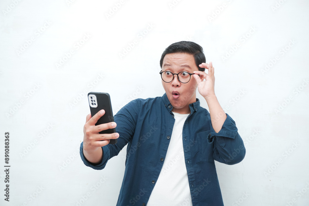 Young Asian man looking smartphone with shocked and surprised expression. Male with blue t-shirt showing excited expression isolated on white background Young Asian man looking smartphone with shocked and surprised expression. Male with blue t-shirt showing excited expression isolated on white background