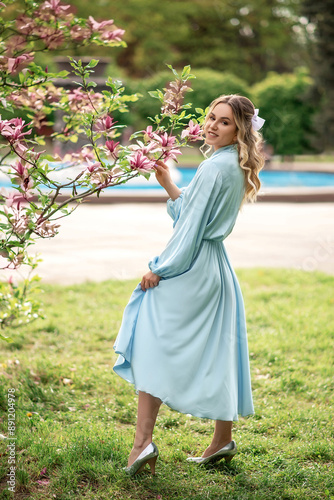 Woman in a light blue dress poses next to a blooming magnolia tree in a park