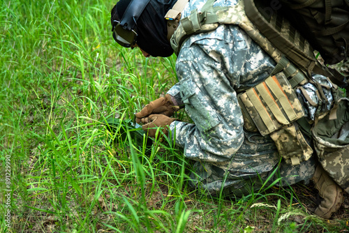 A soldier in camouflage sets a tripwire in the forest photo