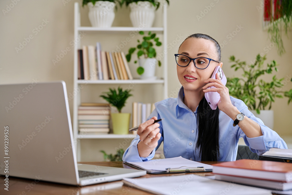 Business woman talking on mobile phone sitting at desk with computer Business woman talking on mobile phone sitting at desk with computer