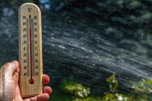 Tableau sur toile A man holds a wooden thermometer in his hand in the garden which indicates a ver