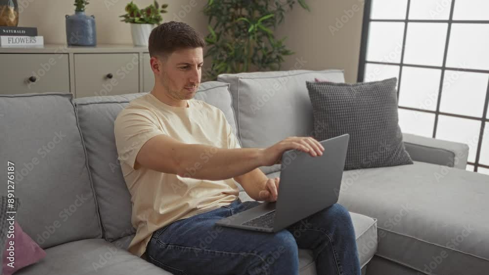 Young hispanic man closing laptop and smiling to camera while sitting on a couch in a modern living room. Young hispanic man closing laptop and smiling to camera while sitting on a couch in a modern living room.