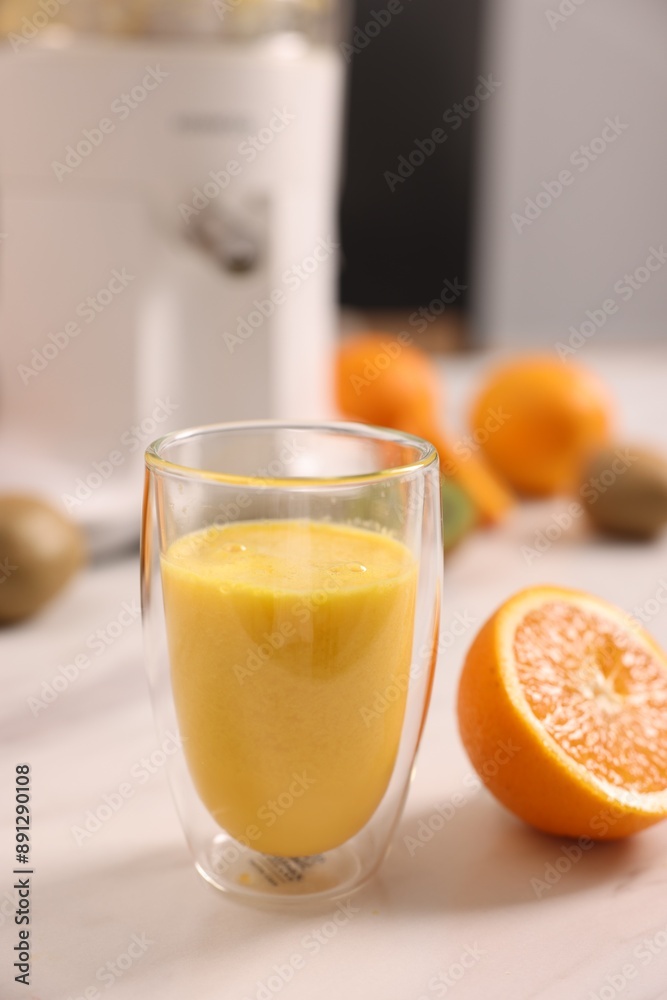 Glass of fresh juice, modern juicer and fruits on white marble table in kitchen, selective focus