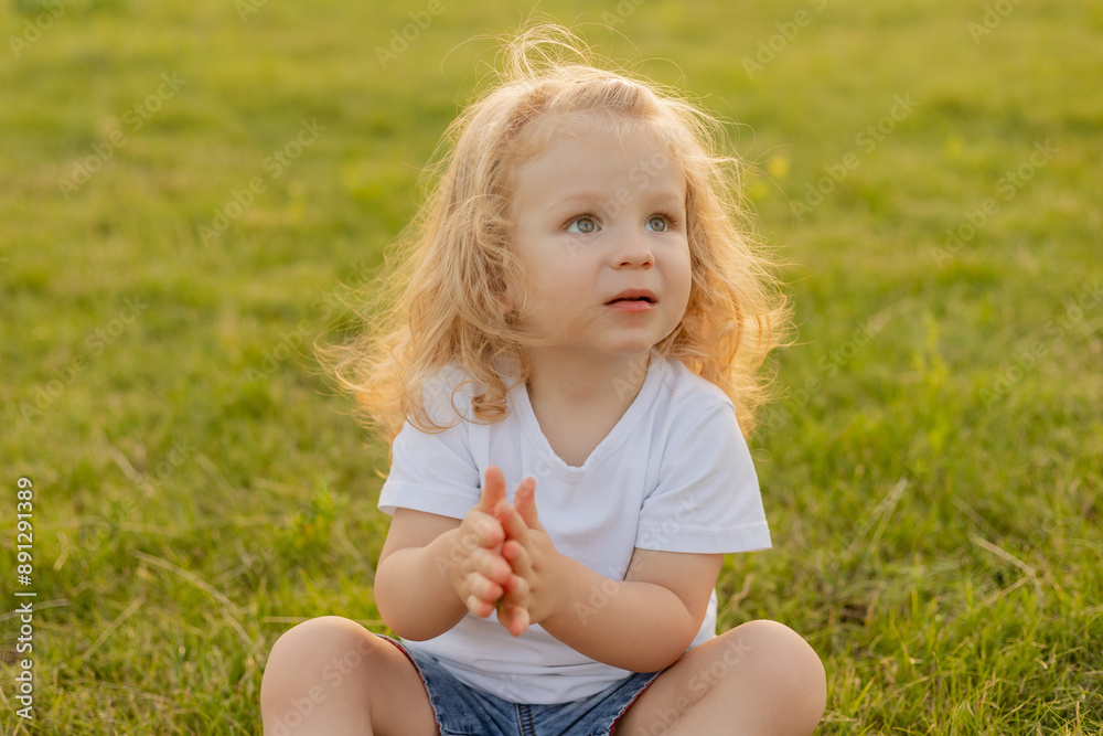 Cute blonde kid with curly hair walks on the lawn with soap bubbles in summer