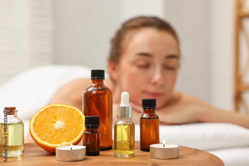 Aromatherapy. Woman relaxing on massage couch in spa salon, focus on bottles of essential oils, orange and burning candles Aromatherapy. Woman relaxing on massage couch in spa salon, focus on bottles of essential oils, orange and burning candles