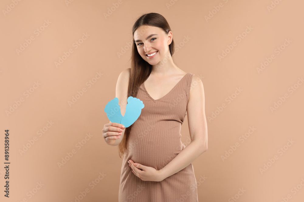 Expecting twins. Pregnant woman holding two paper cutouts of feet on light brown background Expecting twins. Pregnant woman holding two paper cutouts of feet on light brown background