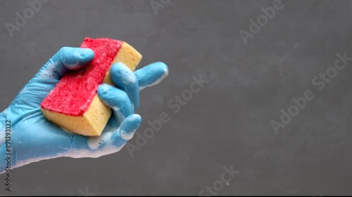 Hand in blue rubber glove squeezes red washing sponge and shows thumb up with soapy foam for cleaning and washing design