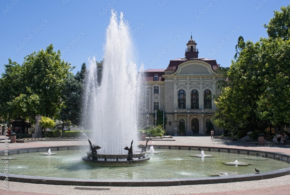 Fototapeta premium Plovdiv, Bulgaria - Jun 30, 2024: Plovdiv city hall. People walking in Ancient Philippopolis on sunday. Streets and buildings. Lifestyle in the urban area. Sunny summer day. Selective focus