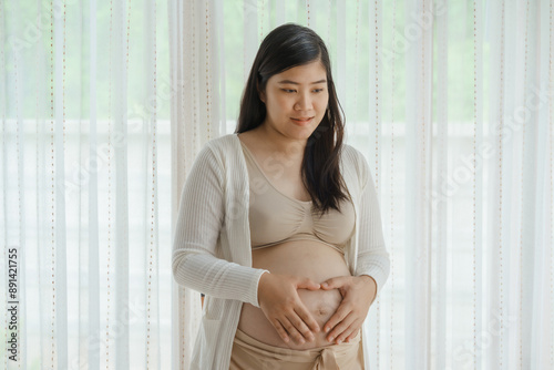 An Asian woman stands while pregnant with her first child, placing her hand on her stomach. She is excited and eagerly waiting for the birth day to meet her baby. Free Download An Asian woman stands while pregnant with her first child, placing her hand on her stomach. She is excited and eagerly waiting for the birth day to meet her baby. - GFXLoad