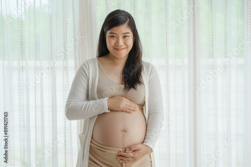 An Asian woman stands while pregnant with her first child, placing her hand on her stomach. She is excited and eagerly waiting for the birth day to meet her baby. Free Download An Asian woman stands while pregnant with her first child, placing her hand on her stomach. She is excited and eagerly waiting for the birth day to meet her baby. - GFXLoad