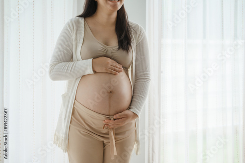 An Asian woman stands while pregnant with her first child, placing her hand on her stomach. She is excited and eagerly waiting for the birth day to meet her baby. Free Download An Asian woman stands while pregnant with her first child, placing her hand on her stomach. She is excited and eagerly waiting for the birth day to meet her baby. - GFXLoad