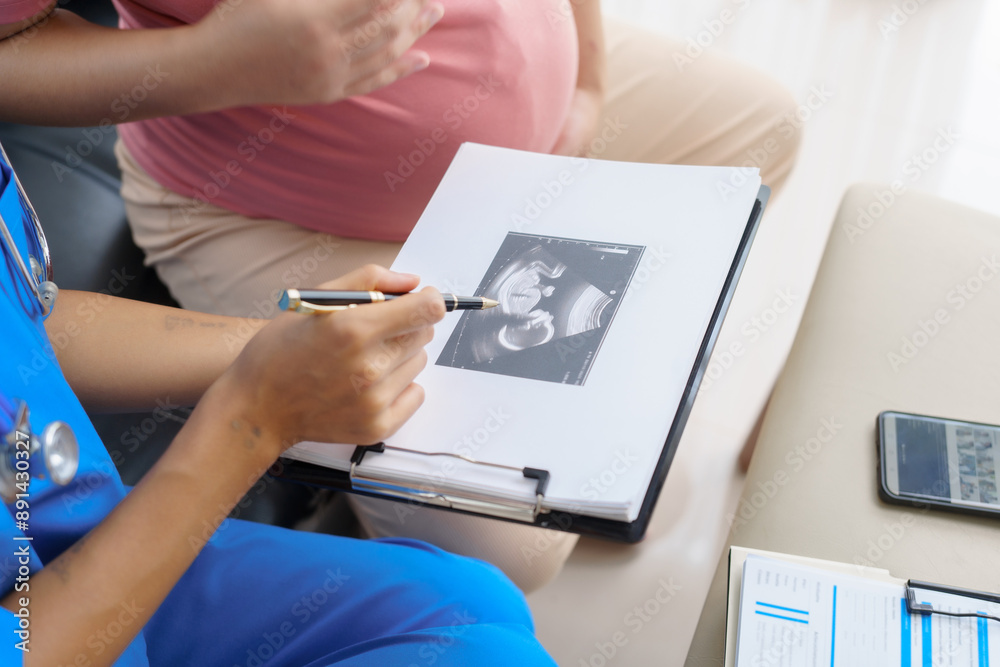 Fototapeta premium Pregnant mothers meet the nurse at the clinic as scheduled, reviewing their medical history and discussing symptoms. Sitting on the sofa, they report headaches, nausea, and back pain to the nurse.