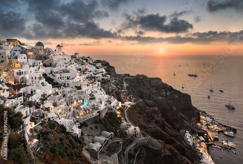 Sunset in Oia village on Santorini, Greece. Famous Santorini sunset capture. Windmills and churches in the background. Blue dome church.