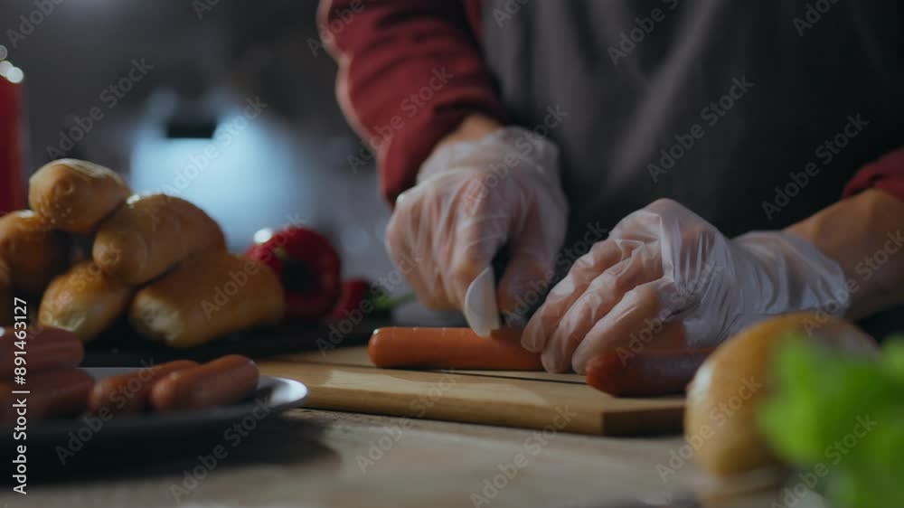 Chef's hands preparing hot dogs. The process of preparing buns with sausage. The cook's hands prepare sausages from vegetable meat by slicing with a knife. Vegetarian snack food preparation Chef's hands preparing hot dogs. The process of preparing buns with sausage. The cook's hands prepare sausages from vegetable meat by slicing with a knife. Vegetarian snack food preparation