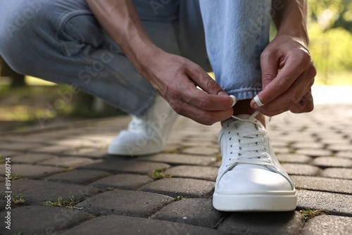 Man tying shoelace of white sneaker outdoors, closeup