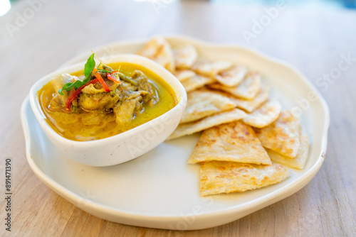 Crispy roti served with green curry with chicken on wooden table
