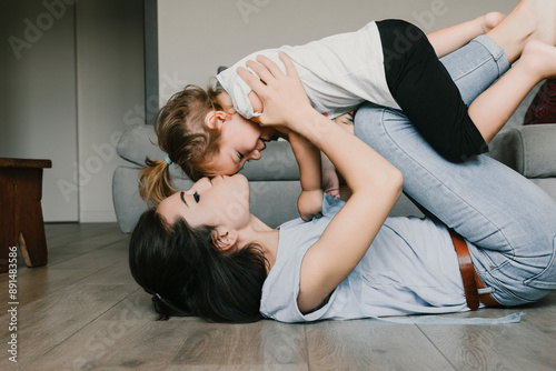 Young mother lying on the floor is playing with her toddler daug photo