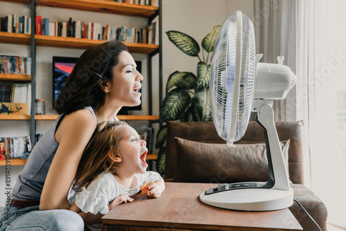 Mother and daughter refreshing at home with electric fan during