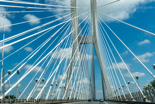 Suspension bridge with cars driving under a bright blue sky with white clouds. High quality photo