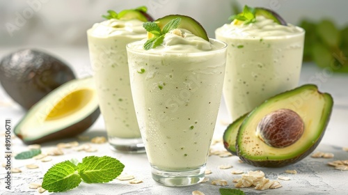 Creamy avocado smoothies garnished with mint leaves, surrounded by fresh and sliced avocados on a white background.