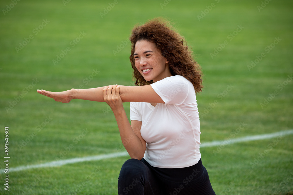 Curly beautiful Asian girl in a white T-shirt and black leggings plays sports on the football field Curly beautiful Asian girl in a white T-shirt and black leggings plays sports on the football field