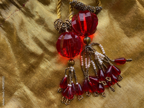 A big red bead with intricate golden and white beads latkans on golden fabric is a striking and elegant embellishment often used in traditional and festive attire.