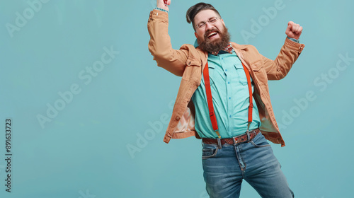 A cheerful, fashionable, and stylish bearded chubby man having fun against a vivid light blue background. The funny man in a bright shirt with a bow tie, jacket, jeans, and suspenders is dancing