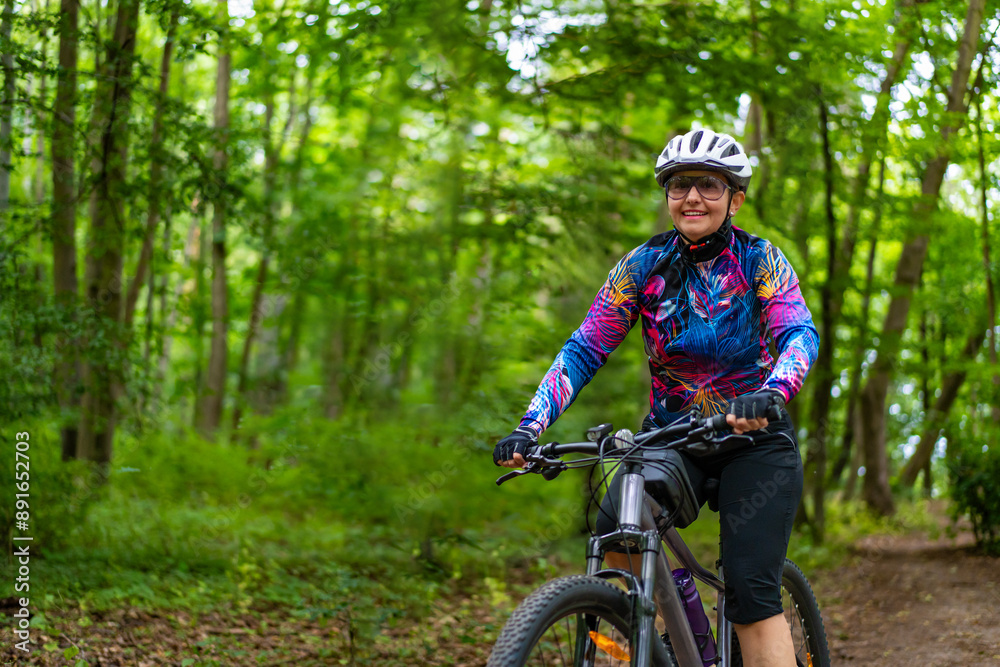 Obraz premium Cycling training in city. Young joyful woman in white helmet and colorful blouse and black shorts riding bike on bike path in city. Playing sports outdoors in spring. Healthy lifestyle 