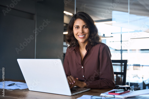 Portrait 30s latin hispanic business woman manager working on laptop computer in modern office. Smiling Indian young businesswoman professional entrepreneur using pc app at workplace looking at camera photo