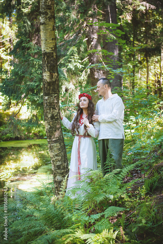 Couple in traditional Slavic clothing embraces in a serene forest © darkbird