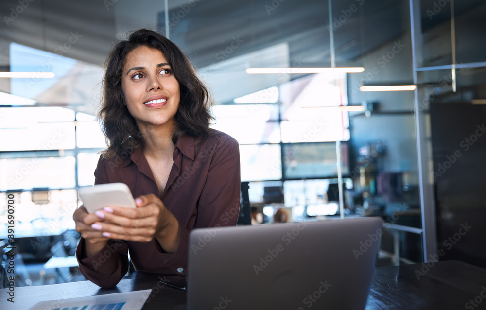 Portrait of young dreaming Indian business woman manager ceo using cell phone mobile app. Pondering Latin Hispanic female businesswoman holding smartphone in office for trading, reading, work online Portrait of young dreaming Indian business woman manager ceo using cell phone mobile app. Pondering Latin Hispanic female businesswoman holding smartphone in office for trading, reading, work online