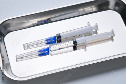 Syringes with needles and an ampoule in a stainless steel medical tray. photo