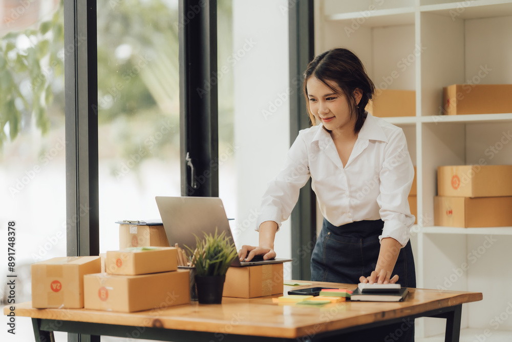 Young female Asian SME business start up online seller owner writing customer address and preparing packages for product.