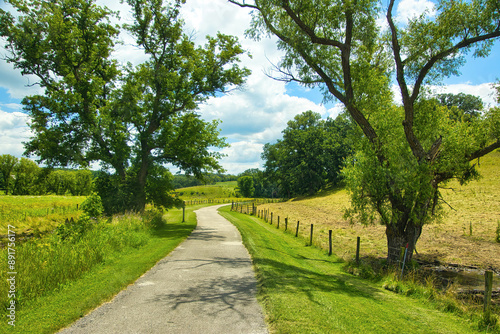 Sunny Summer day landscape of a bike trail passing trees and fenced farm fields along the Root River and Harmony-Preston Valley Trails near Preston, Minnesota.