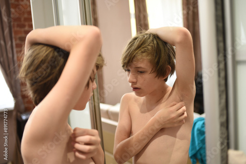 An 11-year-old boy stands in front of a mirror, raised his hand and looks at the hair in his armpit. a teenager explores the changes in his body during puberty.