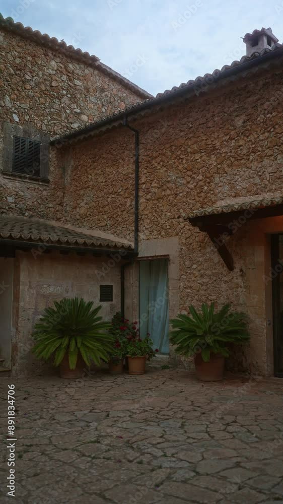 Outdoor view of charming stone house corner with potted plants and rustic architecture under a cloudy sky Outdoor view of charming stone house corner with potted plants and rustic architecture under a cloudy sky