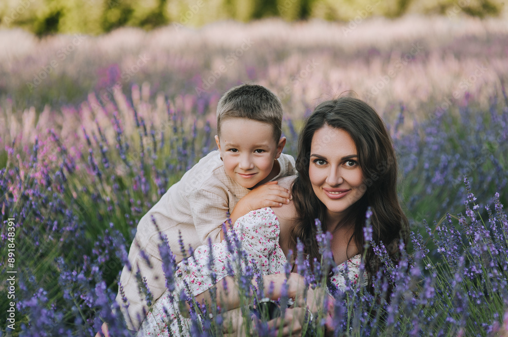 Photo of a happy smiling family, portrait of a beautiful young woman, brunette mother, hugging her beloved son, boy, child in nature against the backdrop of blooming lavender outdoors in a field. Photo of a happy smiling family, portrait of a beautiful young woman, brunette mother, hugging her beloved son, boy, child in nature against the backdrop of blooming lavender outdoors in a field.
